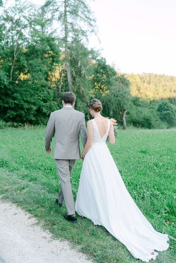 A bride and groom walk through a field in the countryside of Switzerland.