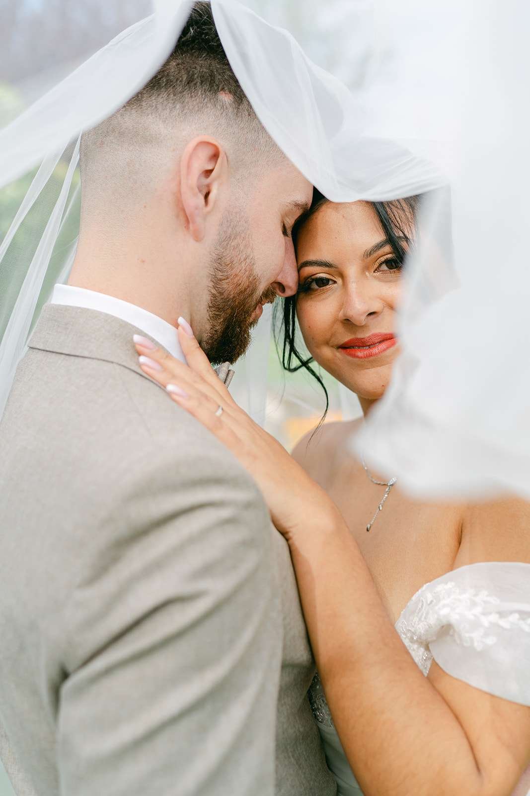 Newlyweds snuggle under the veil with big smiles