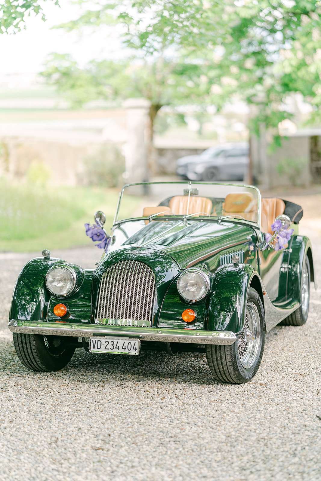 A vintage green roadster parked in a gravel driveway for a wedding