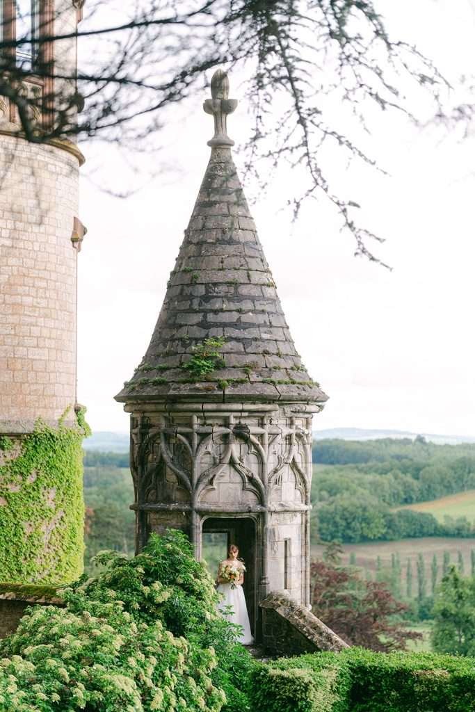 A bride stands in a steeple admiring her bouquet at her Domaine de Bournel wedding