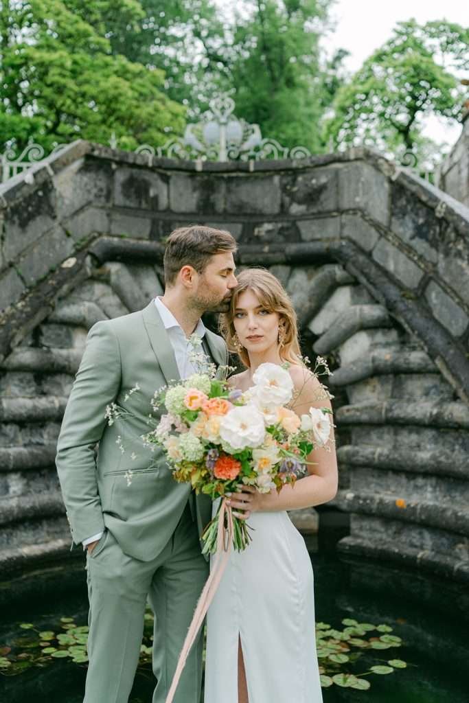 A groom kisses the head of his bride while they stand by a fountain at Domaine de Bournel