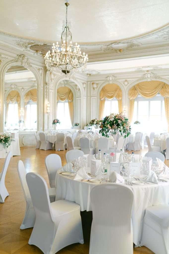 A peak into a set up wedding reception with white linens and crystal chandelier