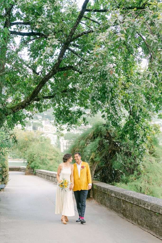 Newlyweds walk holding hands along the walkway of Grand Hotel Suisse Majestic during their wedding