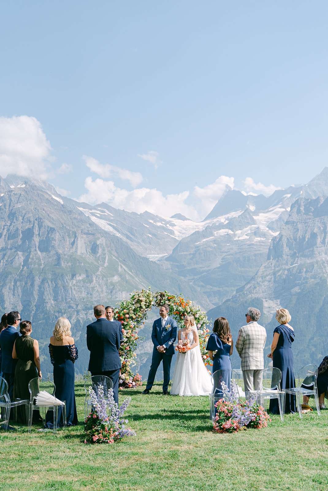 A bride and groom stand under a floral arch during their ceremony with the stunning mountains as their backdrop for their destination wedding in Switzerland