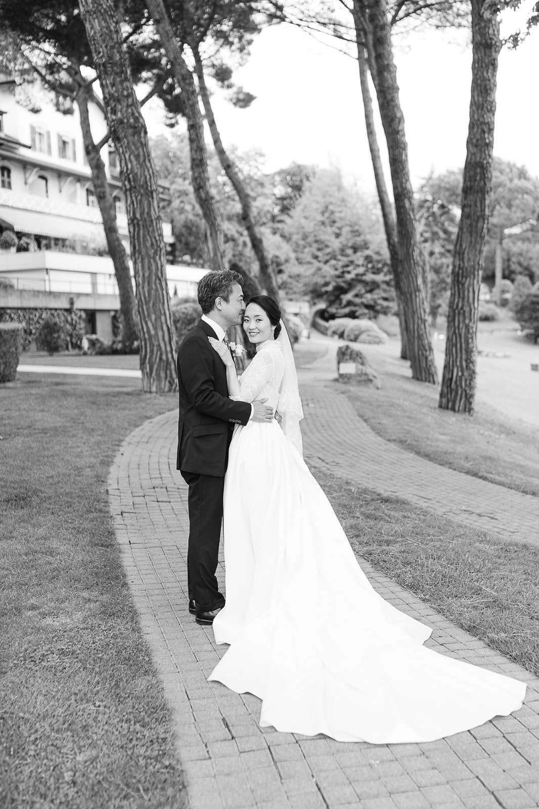 Newlyweds snuggle and smile while walking a brick path through trees at their destination wedding in Switzerland