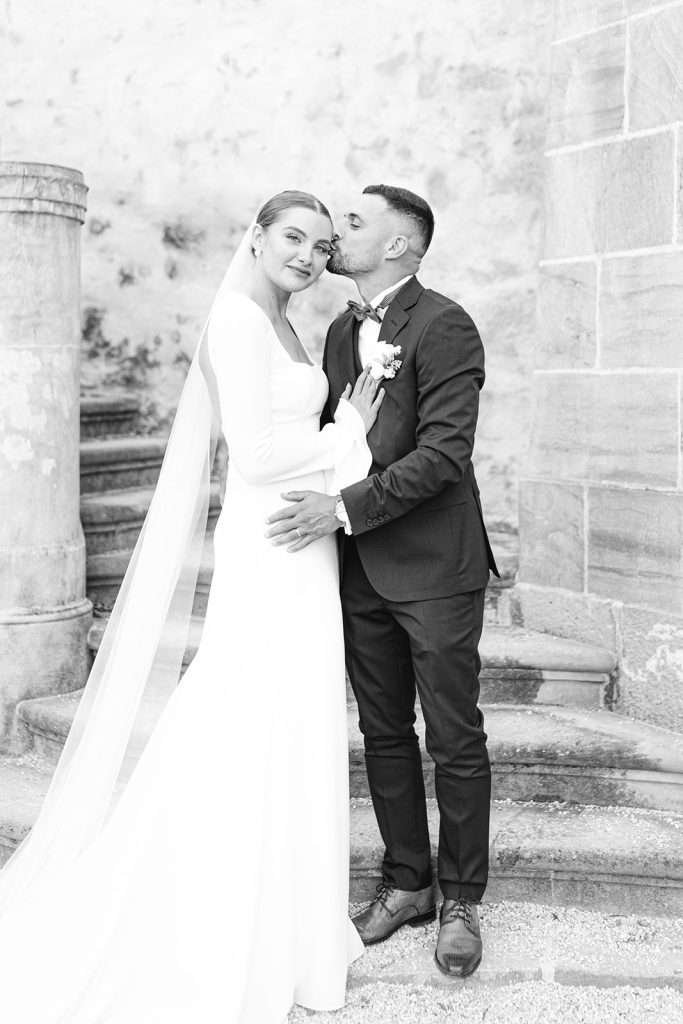 A groom kisses his smiling bride while standing on large outdoor staircase