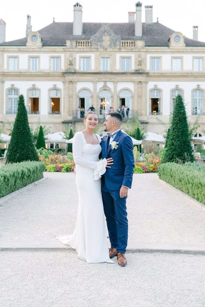 NEwlyweds smile while standing together in the gardens of Hotel du Peyrou